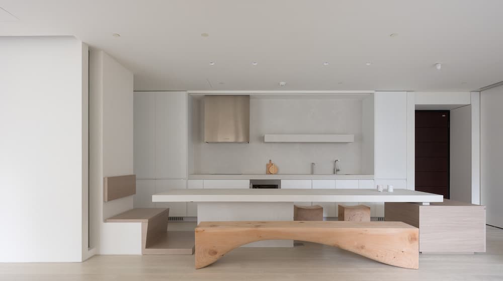 This is a look at the kitchen and dining area with white structures and a wooden bench.