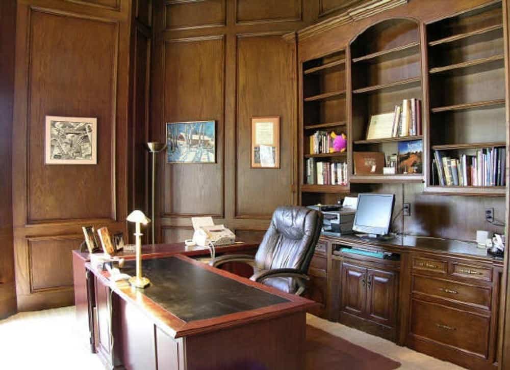 The study has wood-paneled walls, built-in cabinets and shelves, and a wooden desk paired with a leather swivel chair.
