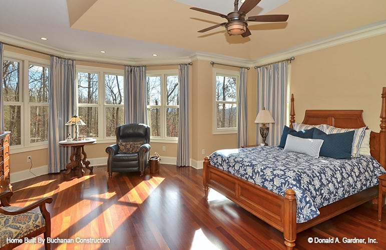 The primary bedroom features a tray ceiling, a cheery sitting area, and a cozy wooden bed that blends in with the hardwood flooring.