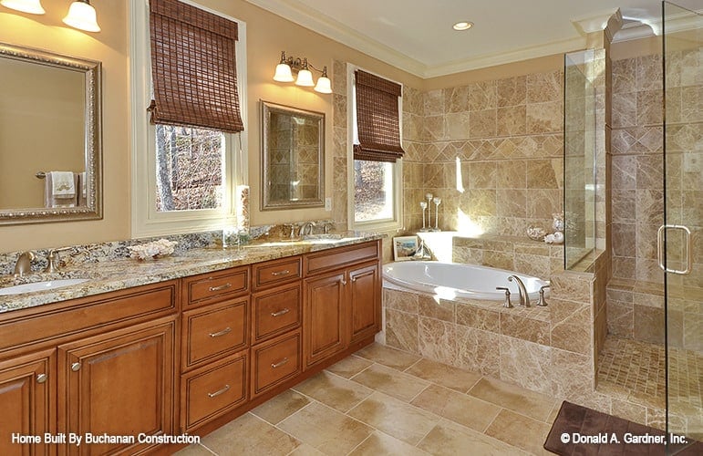 Primary bathroom with a walk-in shower, a drop-in bathtub, and a large wooden vanity equipped with double sinks, intricate mirrors, and warm glass sconces.