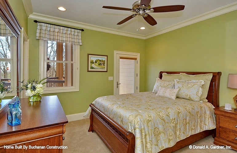 This bedroom has green walls, carpet flooring, wooden furnishings, and a ceiling fan.