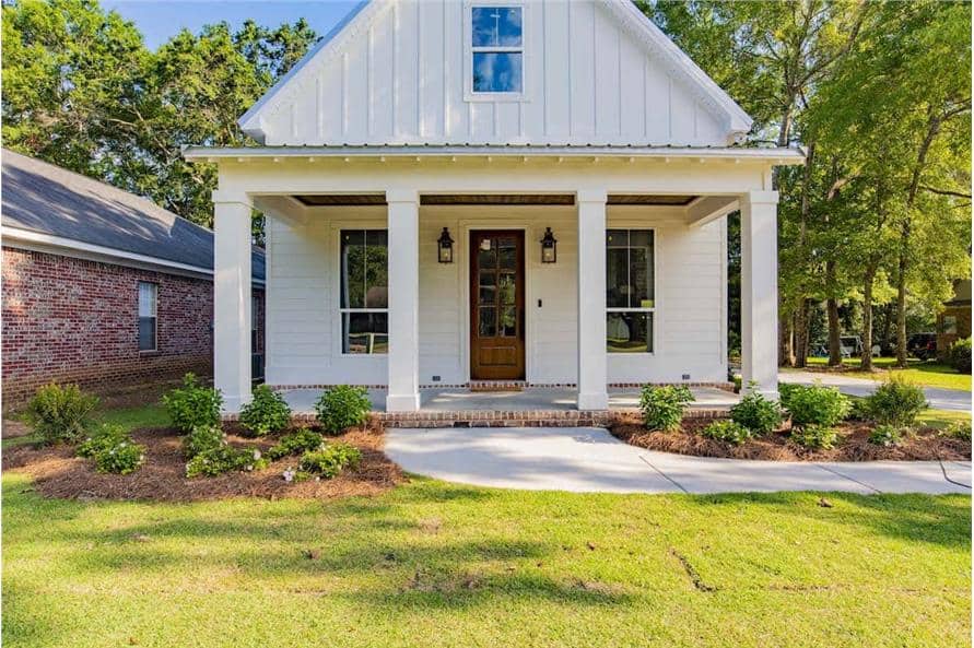 Front exterior view showcasing its board and batten siding, exposed rafter tails, a gable roof, and a covered porch lined with white columns.