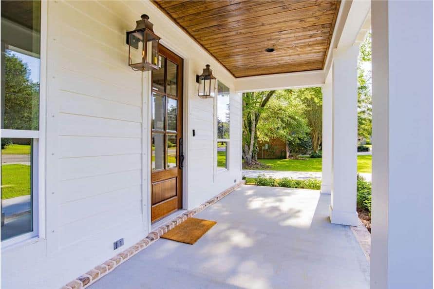 The covered porch includes a wood-paneled ceiling and a glazed entry door flanked by outdoor sconces.