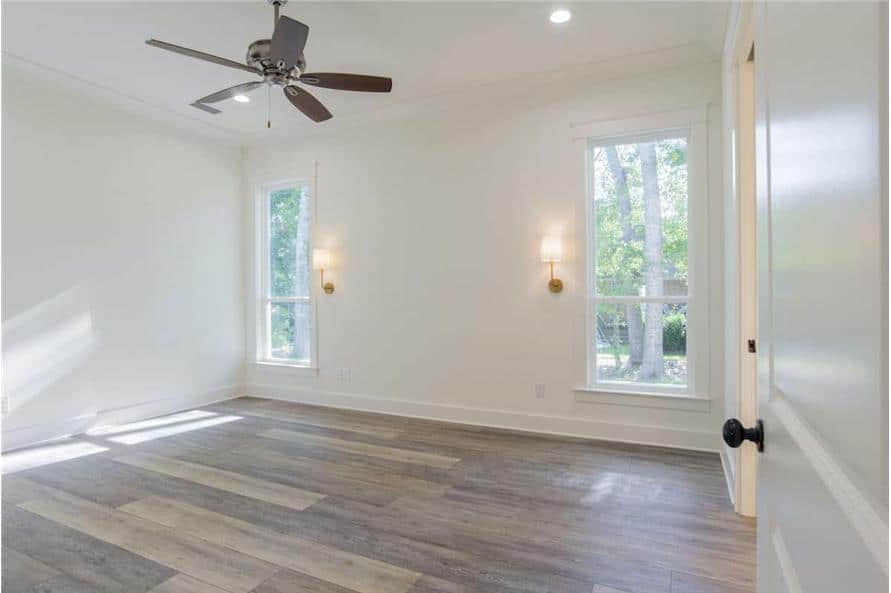 The primary bedroom has hardwood flooring, a ceiling fan, and tall windows complemented with warm glass sconces.