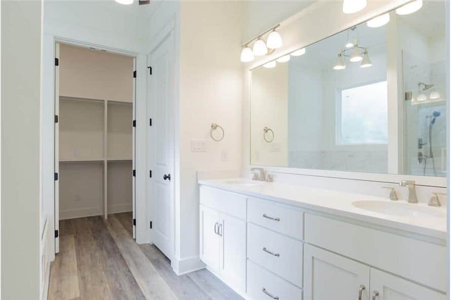 Primary bathroom with a walk-in closet and a large vanity equipped with double sinks, a rectangular mirror, and glass sconces.