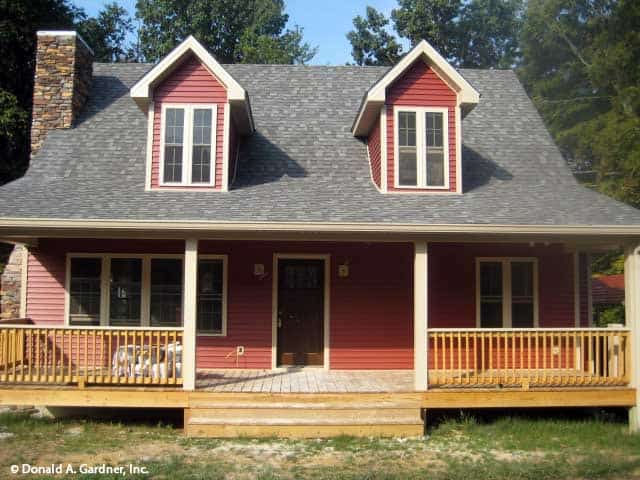 A closer look at the covered entry porch with a wooden stoop, matching railings, and twin dormers resting on its top.
