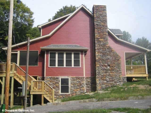 Side exterior view with stone chimney, white-framed windows, and a wooden staircase leading to the rear porch.
