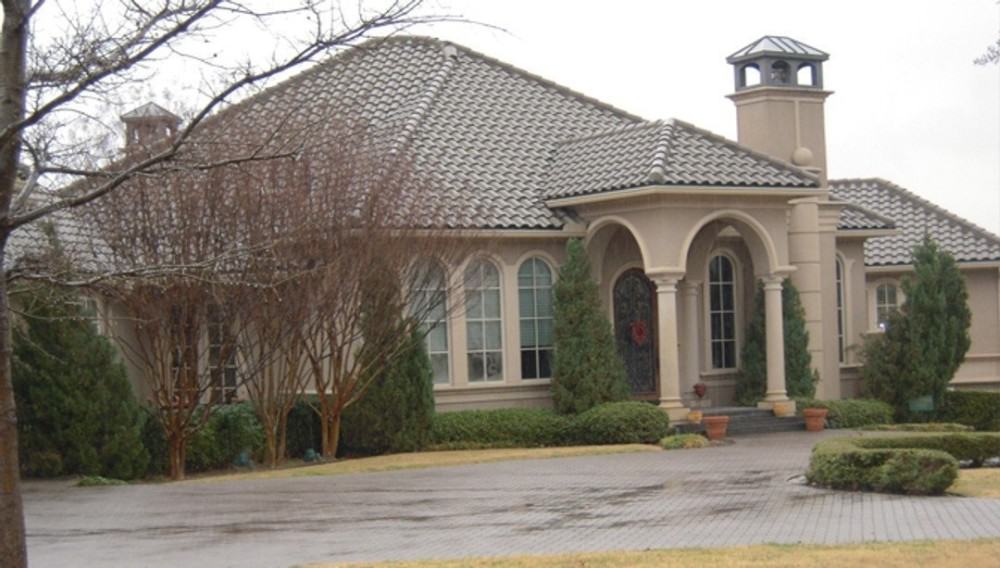 Angled front view showing the entry porch, cupola, arched windows, and clay-tiled roofs.