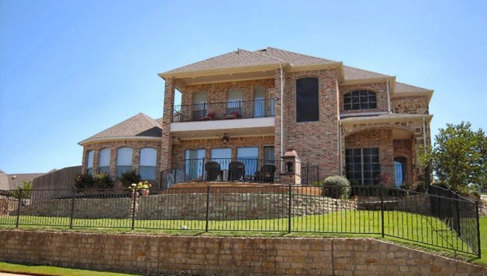 A view of the house from the backyard shows its covered porch, airy patio, and upper balcony bordered with wrought iron railings.