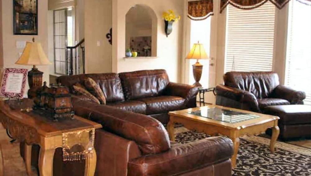 The family room offers brown leather seats, wooden tables, and a patterned area rug.