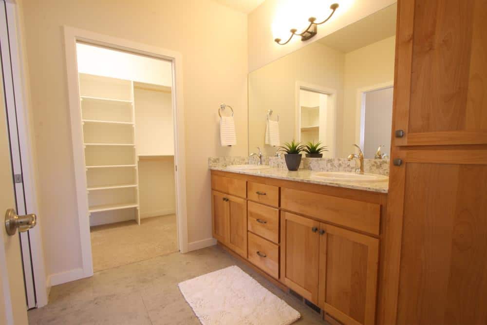 Primary bathroom with a walk-in closet and a dual sink vanity paired with a large frameless mirror.