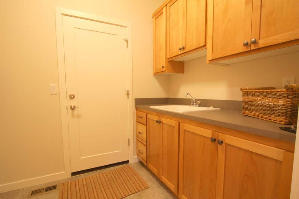 The laundry room is filled with wooden cabinets, a utility sink, and a striped rug that lays on the concrete flooring.