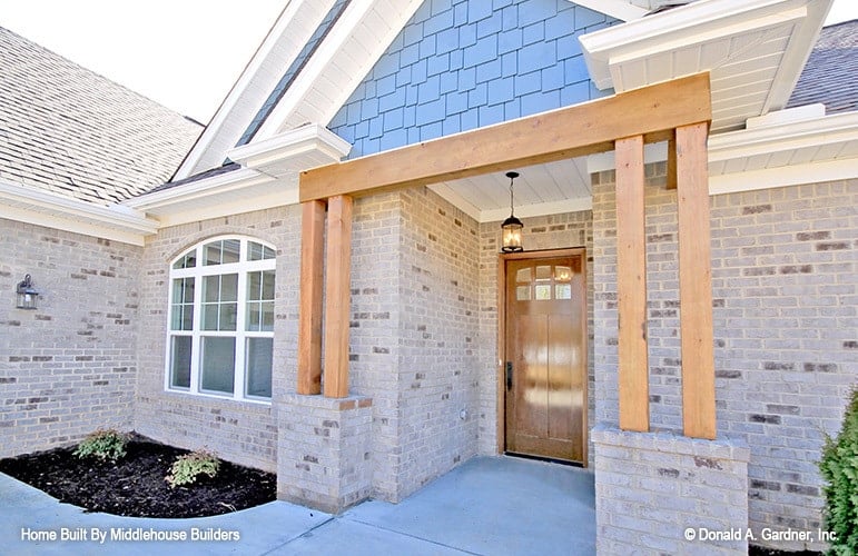 Home entry with double columns and a wooden front door illuminated with a warm glass pendant.