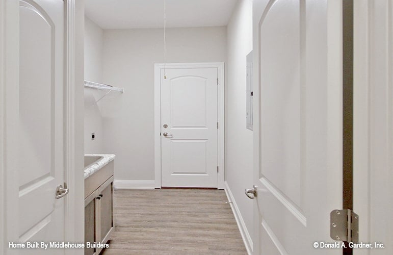 Laundry room with hardwood flooring, a utility sink, and a wall-mounted rack.