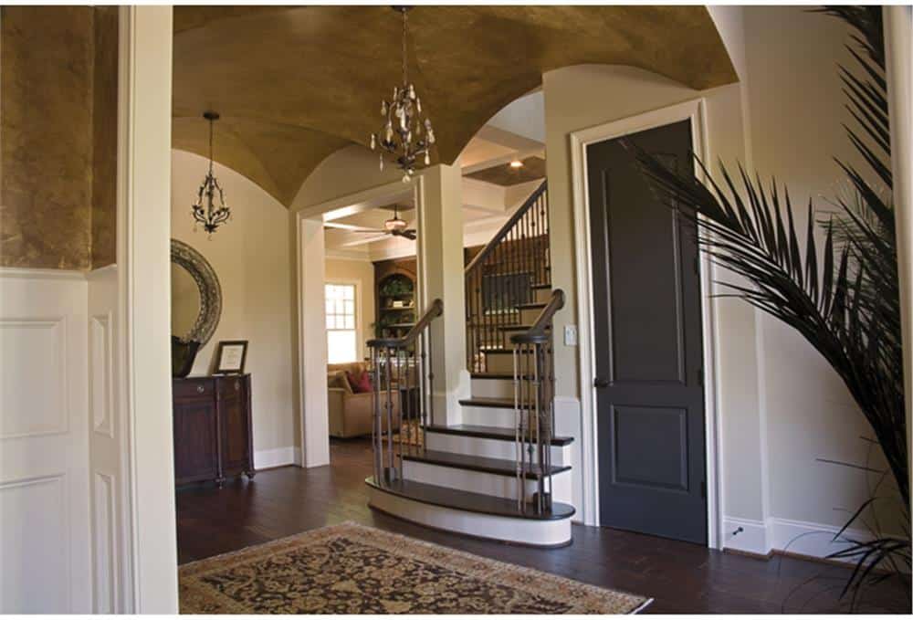 The foyer has a groin vault ceiling, a staircase, and a bordered area rug that lays on the hardwood flooring.