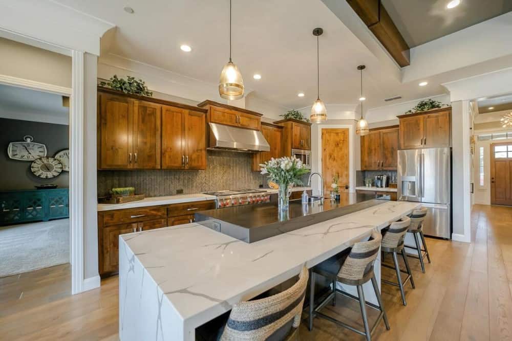 The kitchen offers wooden cabinetry, stainless steel appliances, and a large breakfast island with a marble eating bar.