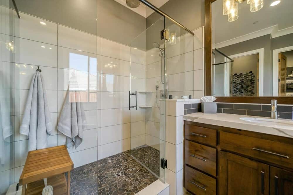 The walk-in shower includes a glass-hinged door and chrome fixtures fitted against the white tiled walls.