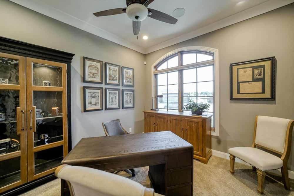 Study with leather chairs, a dark wood desk, display cabinet, and a wooden console table placed against the arched window.