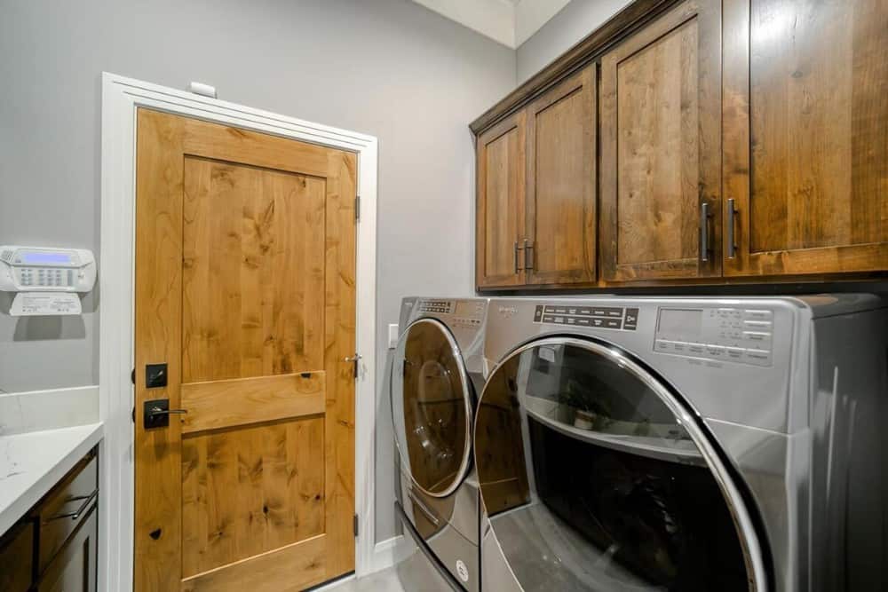 Front-load washer and dryer under overhead cabinets complete the laundry room.