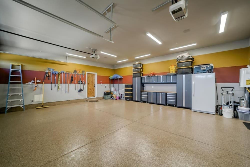 The garage is filled with a ladder, rolling cabinets, storage boxes, a fridge, and tools mounted on the multicolored walls.