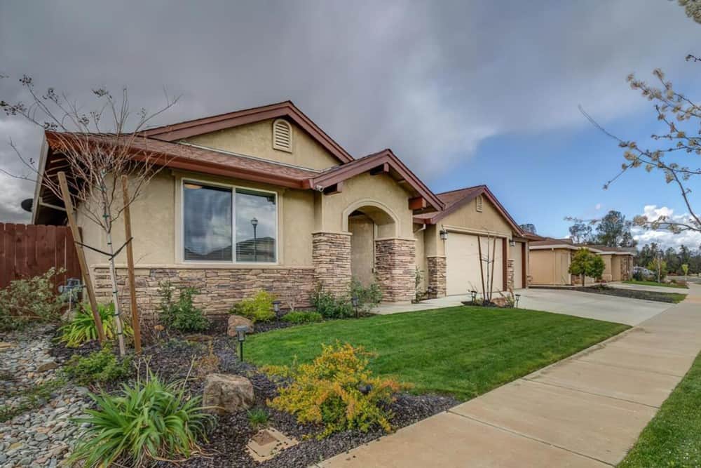 Front-left exterior view with stone and stucco siding, gable rooflines, and an arched entry.