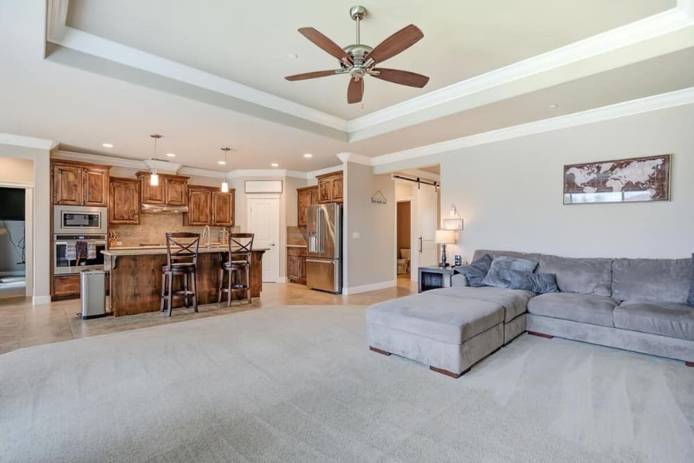 Great room with carpet flooring, an L-shaped sectional, and a tray ceiling mounted with a ceiling fan.