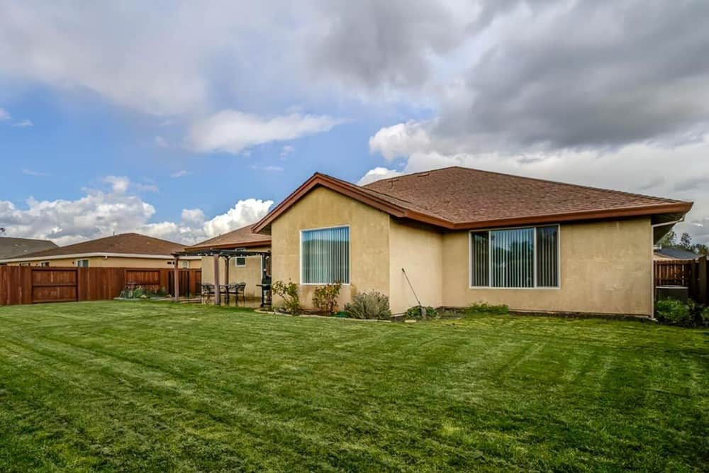 View of the house from the backyard showing its breezy patio and an expansive lush lawn that complements the home's stucco exterior.