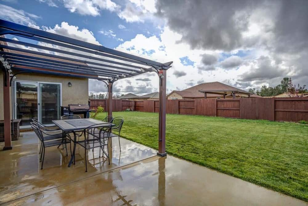 Rear patio with a grill and outdoor dining set under a trellis roof.