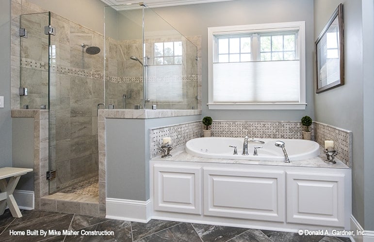 Primary bathroom with a walk-in shower and drop-in bathtub placed under the white-framed window.
