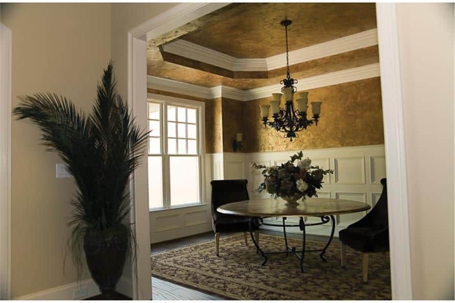 The formal dining room has half-wainscoted walls, a step ceiling, and a round dining set topped with an ornate chandelier.