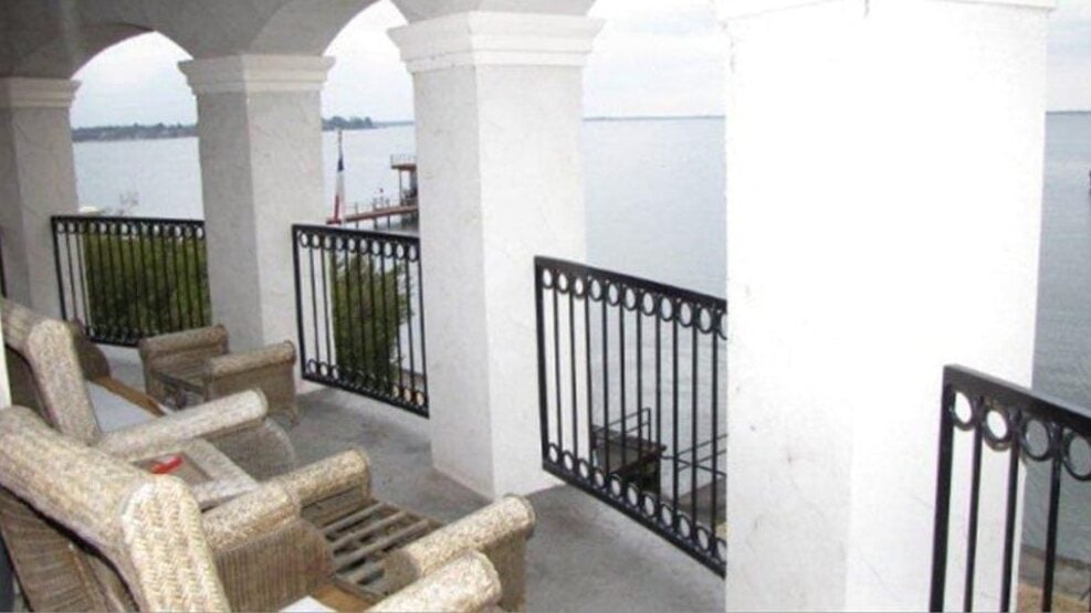 Larger balcony with wicker armchairs, wrought iron railings, and arches overlooking the ocean.