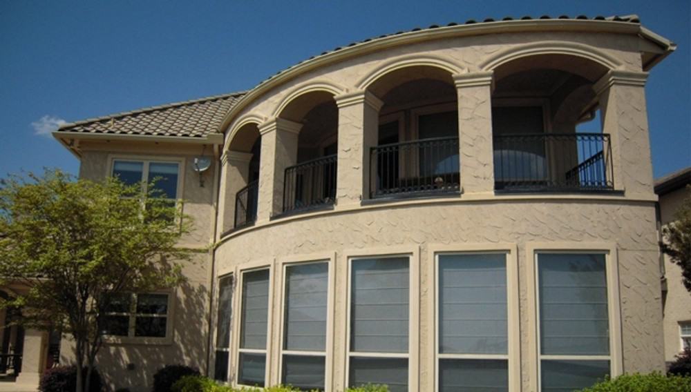 Rear exterior view with textured stucco siding and plenty of arches bordering the upper balcony.