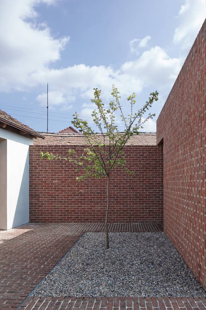 This is a side of the house with a graveled garden and has a small tree in the middle.