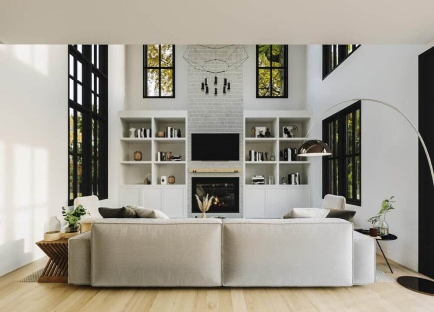 The living room has gray seats, a TV, and a fireplace flanked by white built-ins.