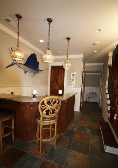 Wet bar with cushioned counter chairs and an angled counter topped with three pendant lights.