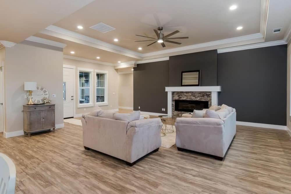 Great room with a tray ceiling, gray sofas, and a stone fireplace fixed against the black accent wall.