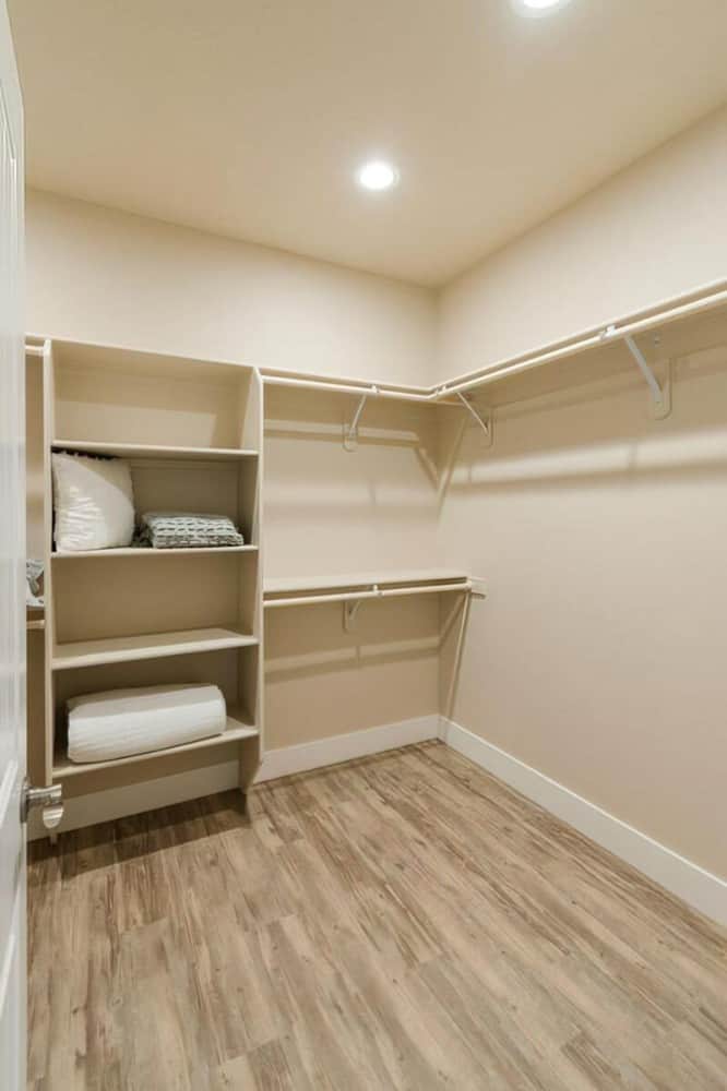 The walk-in closet has hardwood flooring, built-in shelves, and beige walls lined with white base molding.