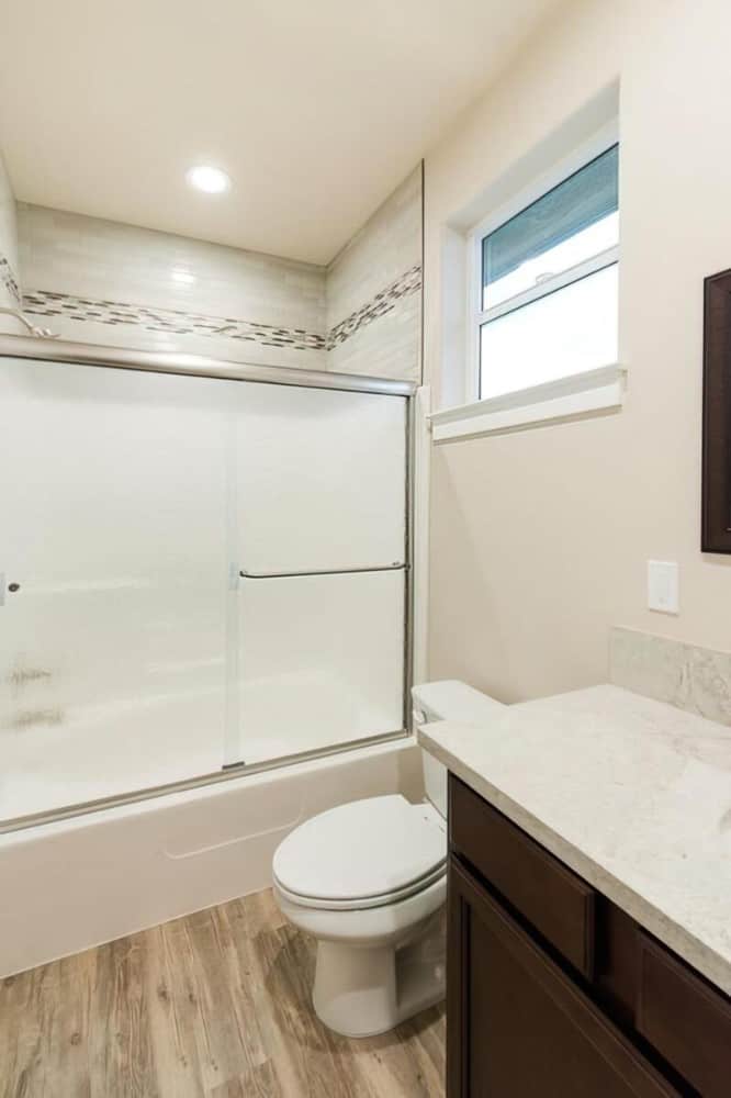 This bathroom offers a dark wood vanity, a toilet, and a tub and shower combo enclosed in sliding glass doors.