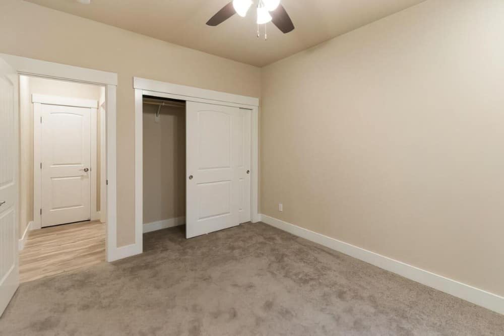 Another bedroom with carpet flooring, a ceiling fan, and a built-in wardrobe with white sliding doors.