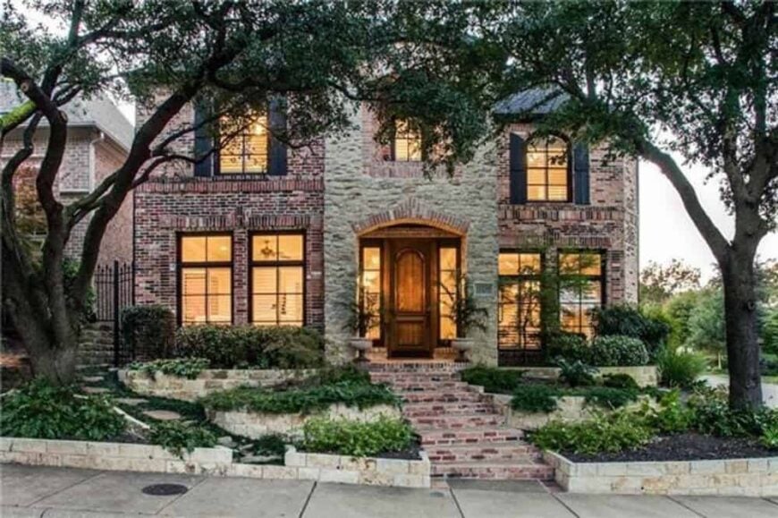 Front exterior view showcasing its stone and brick cladding, shuttered windows, and a covered entry porch accentuated with an arch.