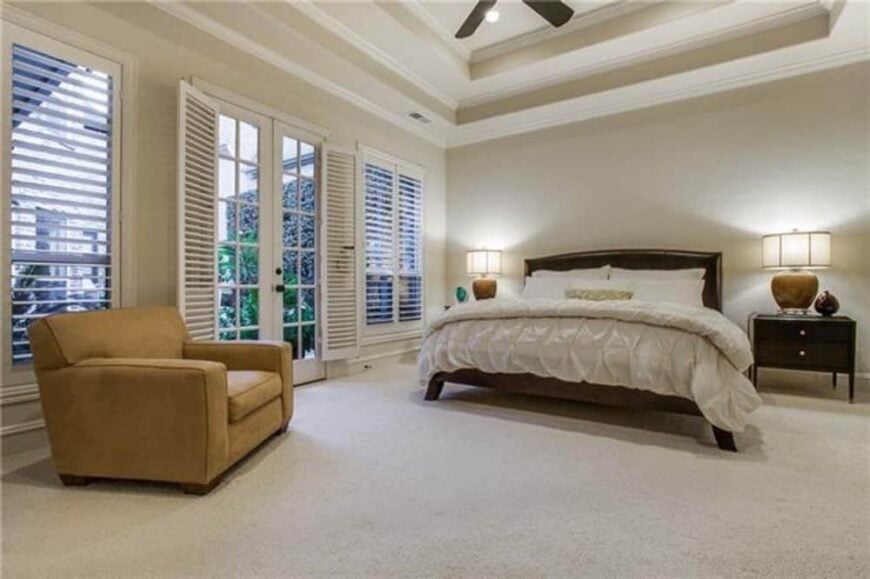 The primary bedroom features a step ceiling, a wooden bed, a leather armchair, and outdoor access via a french door.