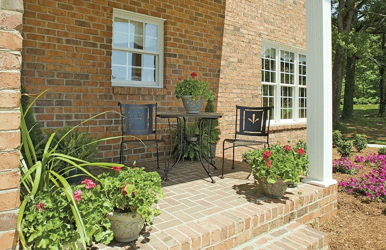 Side exterior view with a covered porch furnished with metal chairs and a matching table.