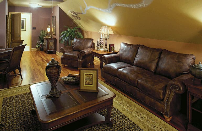 The bonus room is filled with a wooden dining set, a matching coffee table, and brown leather seats under the vaulted ceiling.