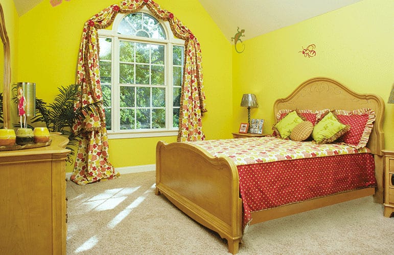 Bedroom with wooden furnishings, yellow walls, a cathedral ceiling, and a Palladian window dressed in floral valances.
