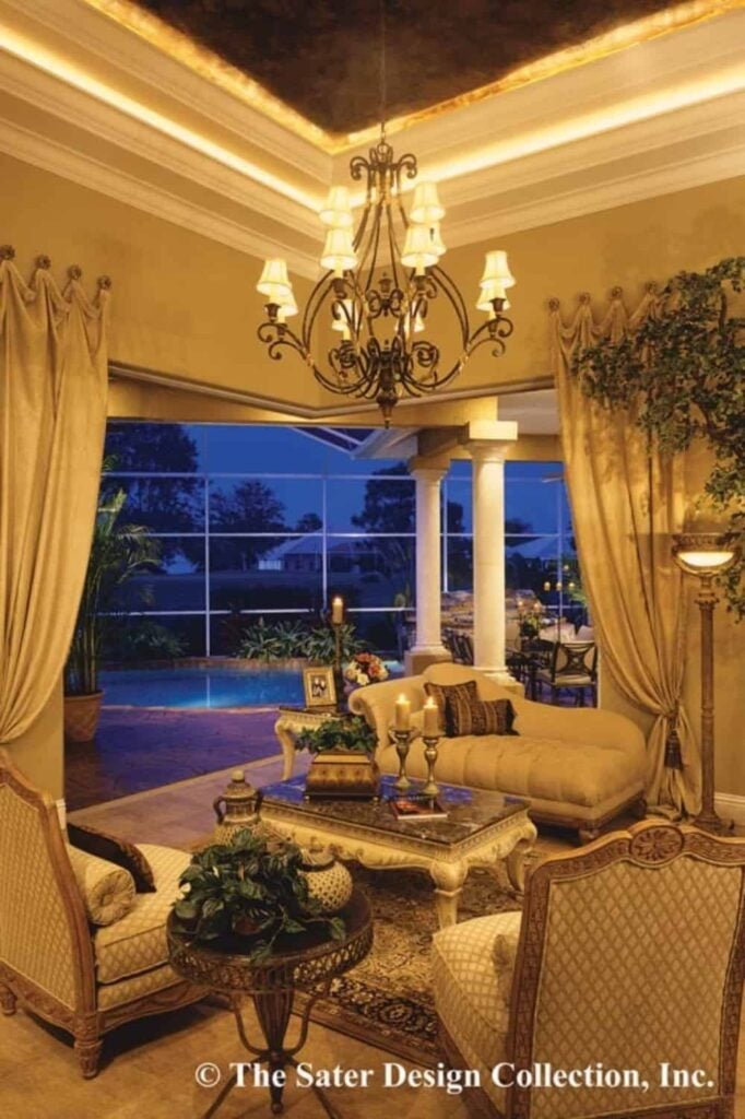Living room with a chaise lounge sofa, patterned chairs, and an ornate wrought iron chandelier hanging from the illuminated step ceiling.