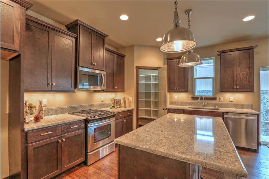 The kitchen is equipped with stainless steel appliances, granite countertops, wooden cabinetry, and a center island topped with chrome dome pendants.