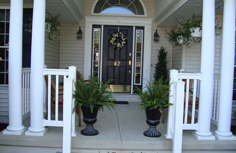 Entry porch with double columns, white railings, and a black front door surrounded by sidelights and an arched transom.
