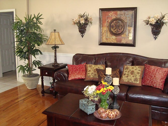 Great room with a leather sectional, dark wood tables, and beige walls graced with white wainscoting and fresh flowers.