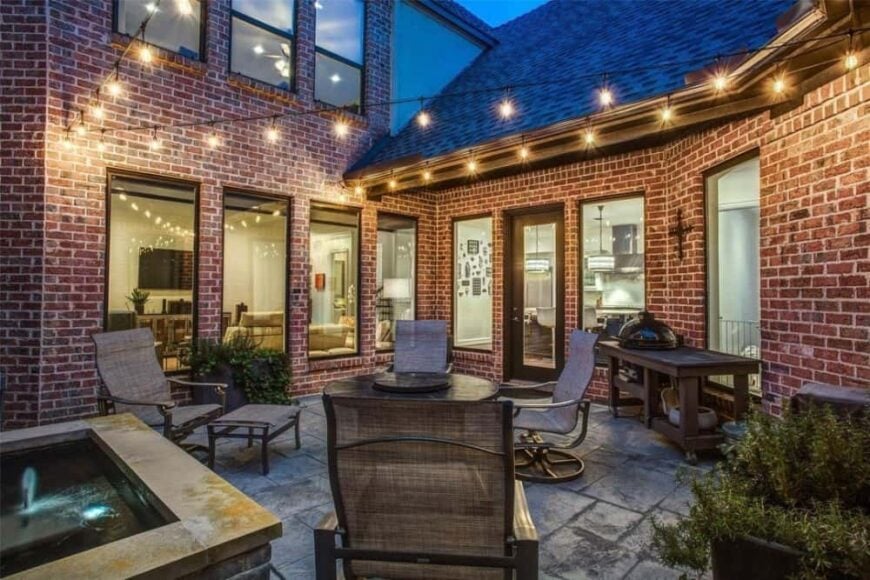 Open patio with woven lounge chairs and a bbq grill illuminated with warm string lights that enhance the cozy ambiance.
