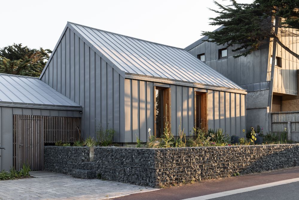 Zinc cladding and roofing house with folding main door, ornamental plants and cobblestone.